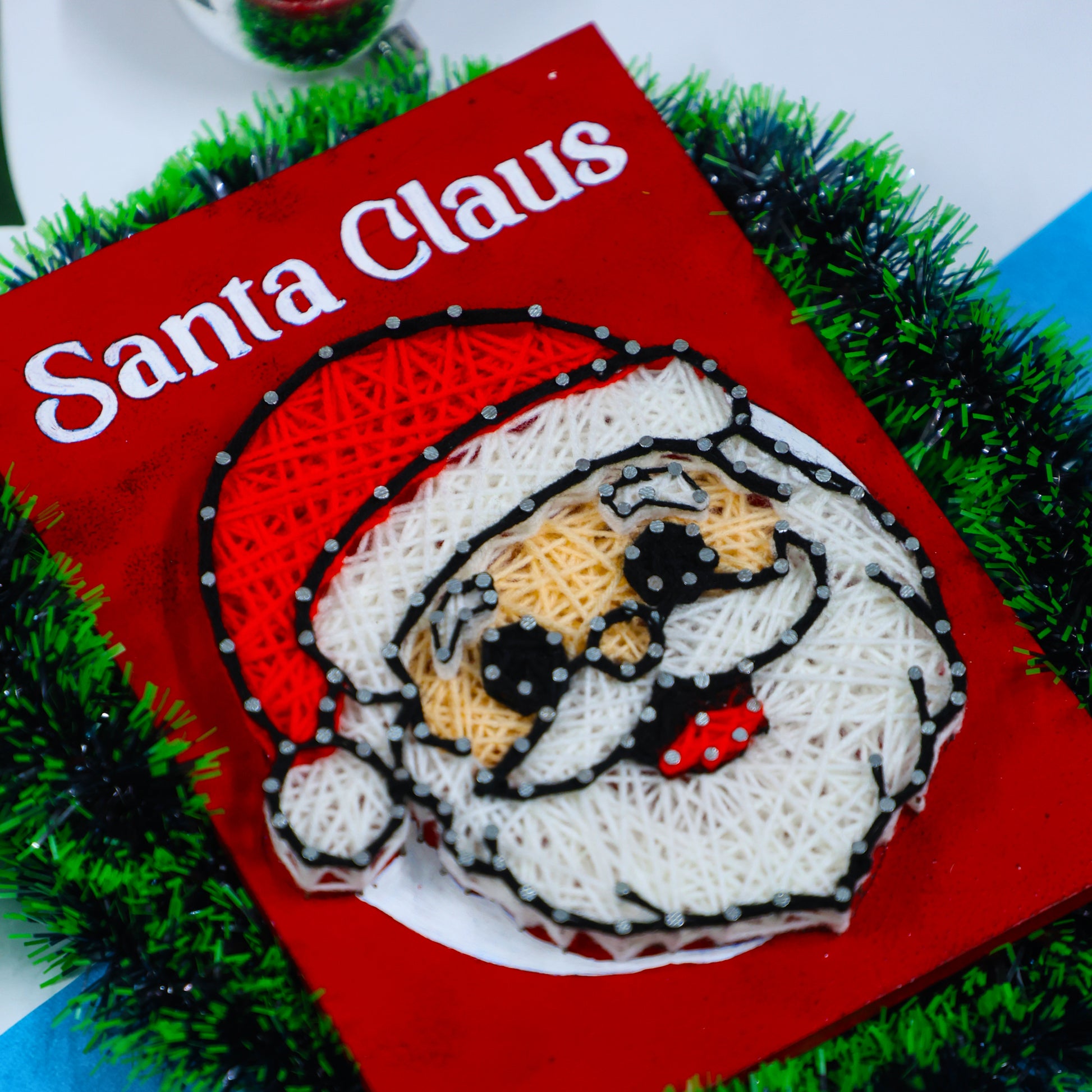 DIY string art of Santa Claus on red canvas – unique handmade Christmas gift or seasonal home decoration.